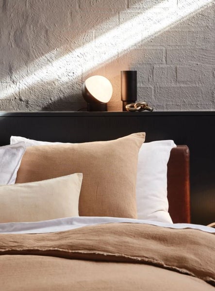 Moderne kugelförmige Tischleuchte mit warmem Licht neben einer hohen Vase und einem dekorativen Kettenglied vor einer strukturierten Wand