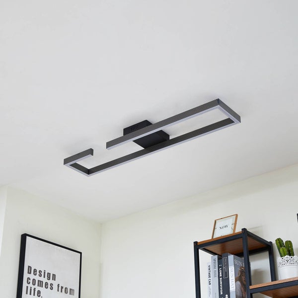 Moderne, rechteckige LED-Deckenleuchte in Schwarz mit gerippter Struktur an einer weißen Decke in einem hellen, organisierten Raum über einem Regal.