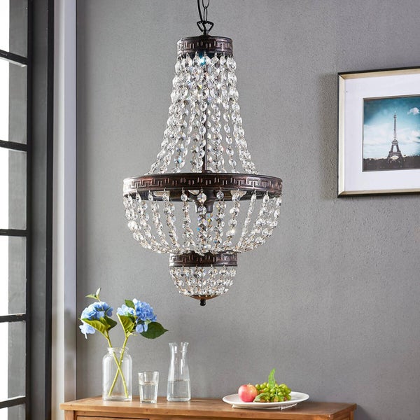 Klassischer Kristall-Kronleuchter mit bronzefarbenem Metallrahmen und griechischem Muster über einem Holztisch in einem eleganten Zimmer.