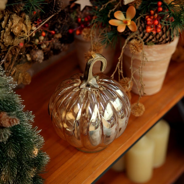 Dekorative Kürbisfigur aus Glas auf einem Holzregal, umgeben von herbstlicher Dekoration.