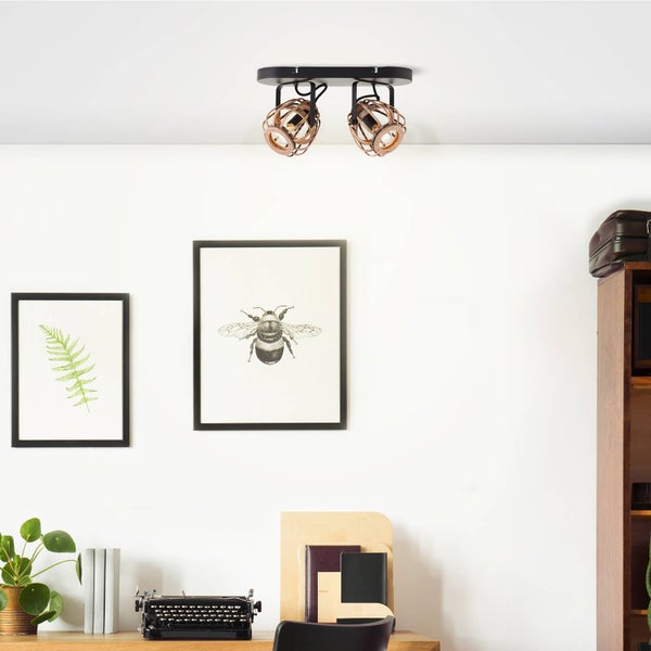 Zweiflammiger Deckenstrahler mit käfigartigen Holzschirmen und schwarzer Metallbasis in einem hellen Arbeitszimmer mit Schreibtisch und Wandbildern.