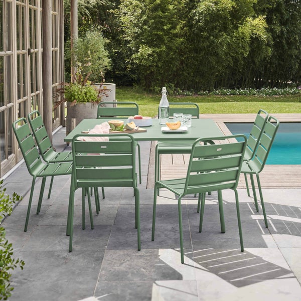 Grünes Gartenmöbel-Set aus Metall mit Tisch und Stühlen auf einer Steinterrasse neben einem Swimmingpool.