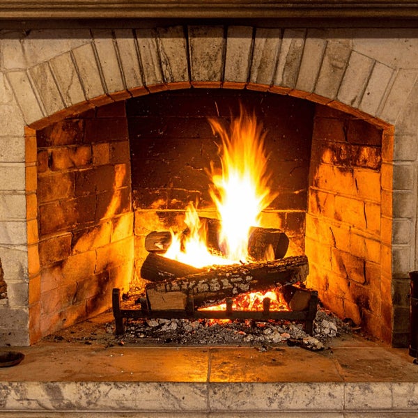 Ein brennender Kamin mit gemauerter Umrandung und loderndem Holzfeuer in einem offenen Feuerraum.
