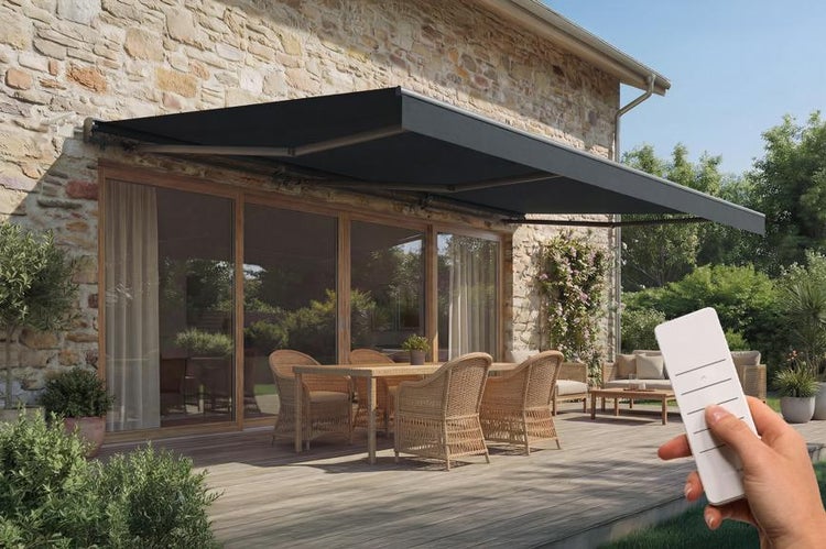 Elektrische Gelenkarmmarkise über einer Terrasse mit Korbmöbeln und Holzboden vor einer Natursteinwand, gesteuert per Fernbedienung.