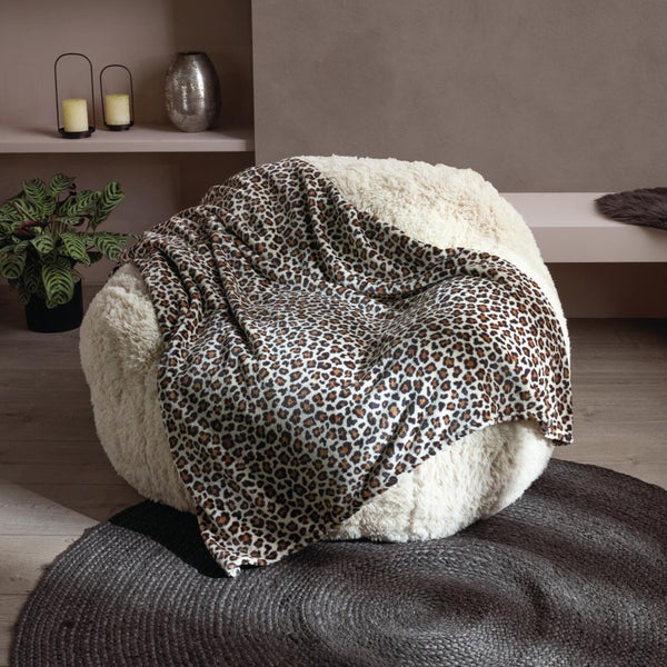 Ein flauschiger Sitzsack mit einer Wohndecke in Leopardenmuster in einem modernen Wohnraum mit Pflanzen und Kerzen.