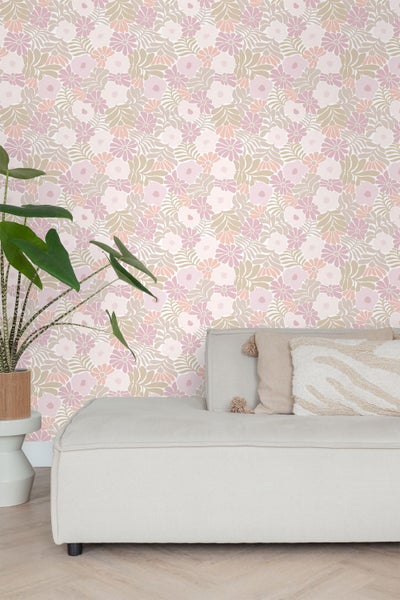 Vliestapete mit floralem Muster aus stilisierten Blumen und Blättern in einem hellen Wohnzimmer mit Sofa und Zimmerpflanze.
