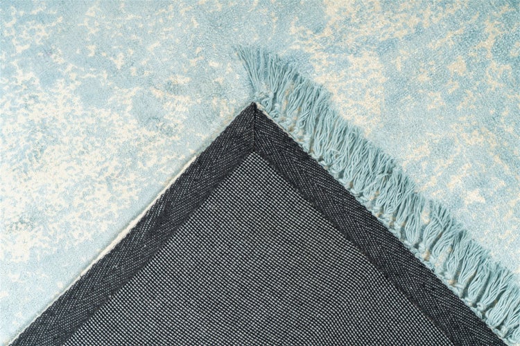 Blauer Teppich mit abstraktem Muster und Fransen, Detail der gewebten Rückseite an einer umgeklappten Ecke.