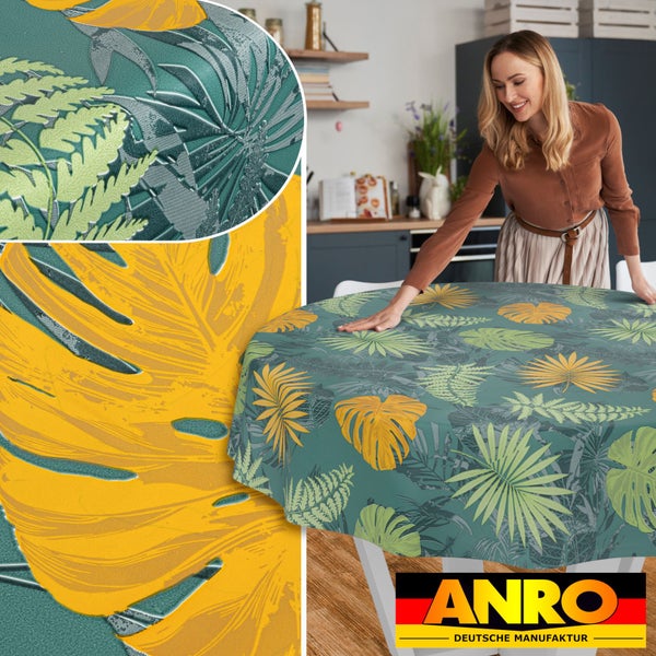 Runde Wachstuch-Tischdecke mit tropischem Blättermuster, von einer Frau auf einem Tisch ausgebreitet. Hergestellt in Deutschland. ANRO Logo.