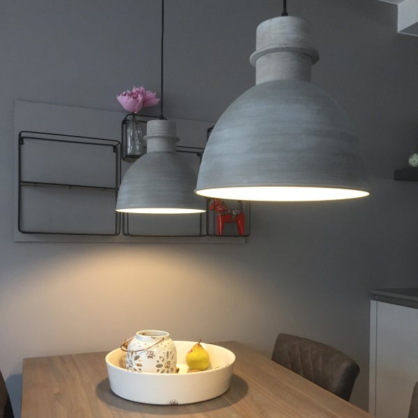 Zwei industrielle Pendelleuchten in Beton-Optik über einem Holztisch mit Dekoration.