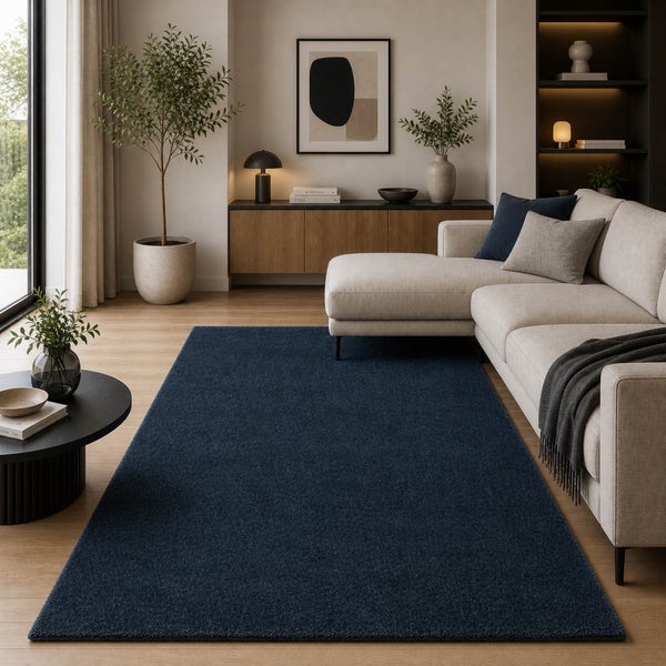 Moderner blauer Teppich in einem hellen Wohnzimmer mit hellem Ecksofa, Sideboard aus Holz und Zimmerpflanzen.