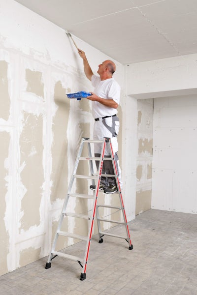 Handwerker auf einer Leiter beim Streichen einer Wand