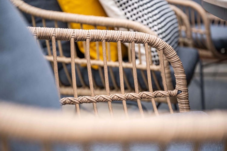 Detailaufnahme eines Gartenstuhls aus Polyrattan Geflecht mit grauen Polstern und dekorativen Kissen