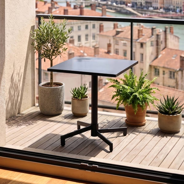 Quadratischer Metall-Bistrotisch auf einem Balkon mit Holzboden und Glasgeländer, umgeben von verschiedenen Topfpflanzen vor einer Stadtkulisse.