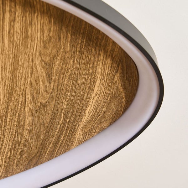 Detailaufnahme einer modernen Deckenleuchte mit Paneel in Holzoptik, weißem Lichtdiffusor und schwarzem Metallrahmen.
