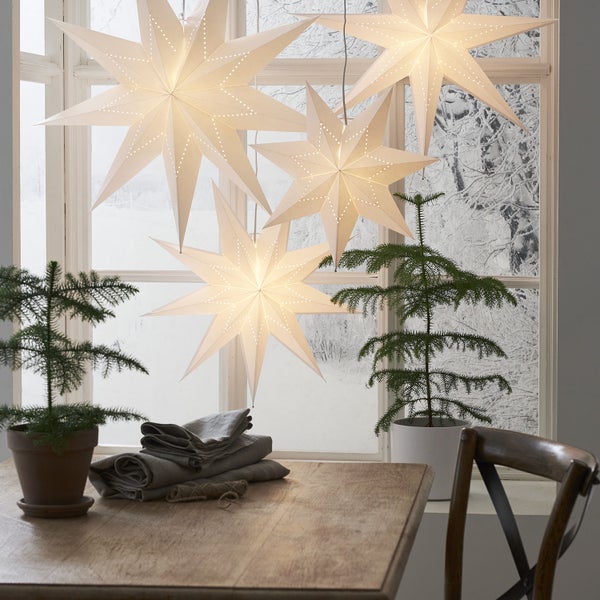 Szene mit beleuchteten Papiersternen, Tisch, Pflanzen und Fenster im Winter.