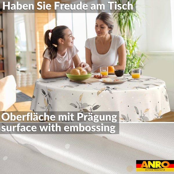 Rundes Tischtuch mit Blattmuster und geprägter Oberfläche, dargestellt in einer Szene mit Familie am Tisch. ANRO Deutsche Manufaktur Logo.