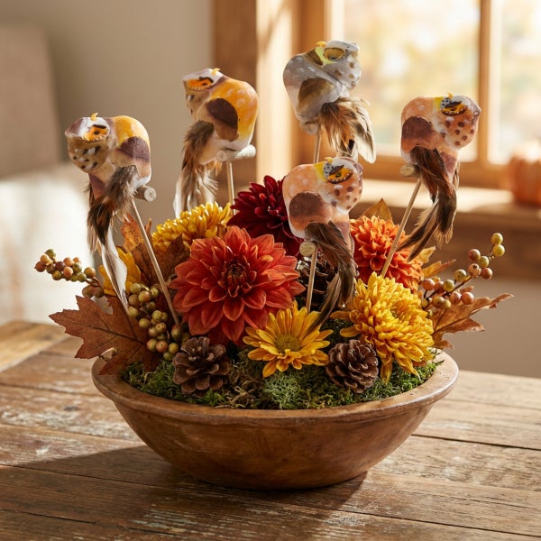 Herbstliche Tischdekoration in einer Holzschale mit Kunstblumen, Tannenzapfen, Beeren, Herbstblättern und künstlichen Vögeln an Holzstäben.