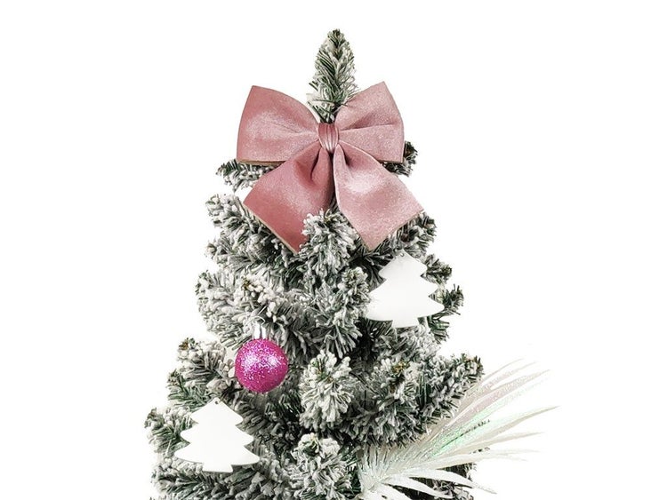 Die Spitze eines künstlichen, verschneiten Weihnachtsbaums geschmückt mit einer Samtschleife, glitzernden Christbaumkugeln und Tannenbaumanhängern.