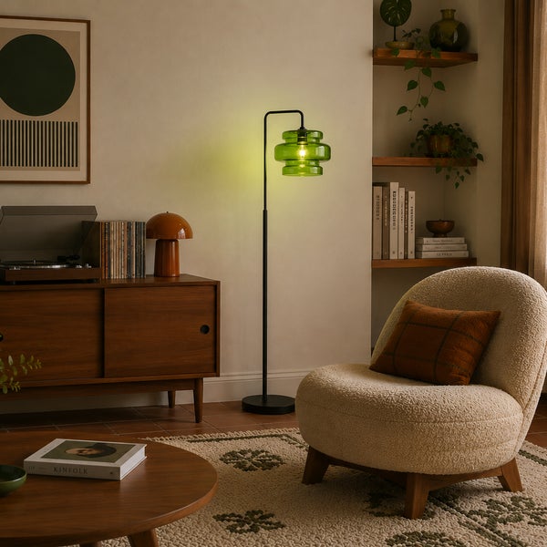 Moderne Stehlampe mit grünem Glasschirm und schwarzem Metallfuß in einem wohnlich eingerichteten Wohnzimmer mit Sessel und Sideboard.