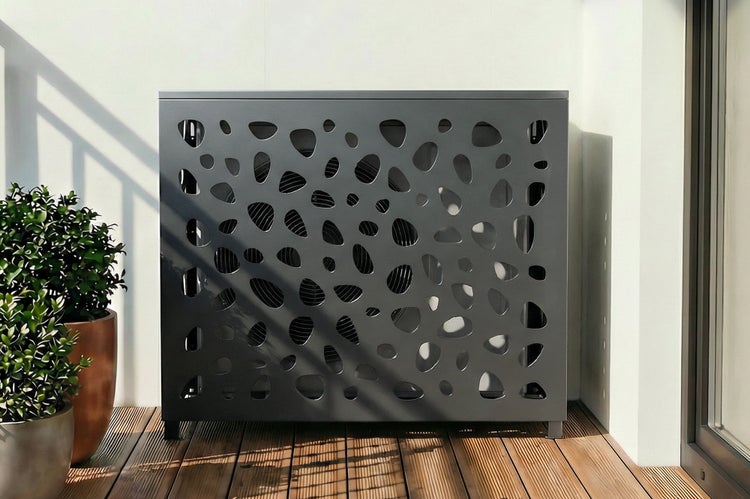 Verkleidung für eine Wärmepumpe mit dekorativem Lochmuster auf einem Balkon.