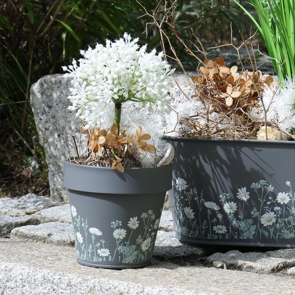 Graue Blumentöpfe mit floralem Gänseblümchen-Muster, bestückt mit dekorativen Kunstpflanzen und Trockenblumen auf Naturstein.