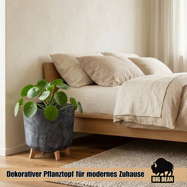 Moderner Pflanztopf mit Holzbeinen in einem hellen Schlafzimmer mit Ufopflanze neben einem Holzbett mit Leinenbettwäsche