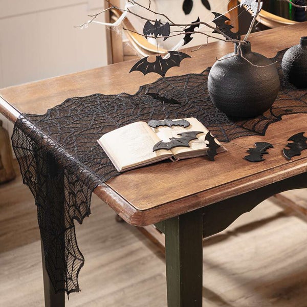 Dekorativer Halloween-Tisch mit Tischläufer im Spinnennetzdesign, Vasen und Fledermausdekoration