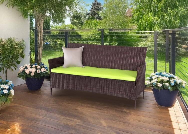 Moderne Zweisitzer Gartenbank aus dunkelbraunem Polyrattan auf einer Holzterrasse mit grüner Sitzauflage und hellem Kissen, helle Atmosphäre.