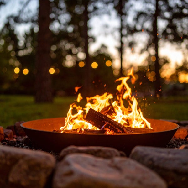 Feuerschale mit brennendem Holzfeuer im Garten vor Waldkulisse bei Dämmerung