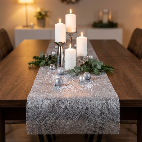 Festliche Tischdekoration mit vier brennenden Kerzen auf Kerzenhaltern, silbernen Kugeln, Tannenzweigen und Tischläufer auf einem Holztisch.