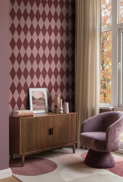 Modernes Wohnzimmer mit Rauten-Tapete in Dunkelrot und Rosa, Holz-Sideboard, lila Sessel und hellem Fenster mit Vorhängen.