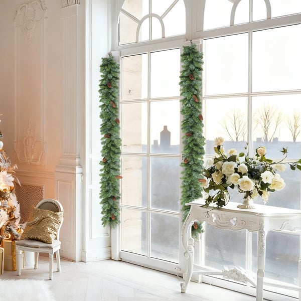 Zwei vertikale grüne künstliche Weihnachtsgirlanden mit Tannenzapfen an einem großen weißen Fenster in einem hellen Raum.