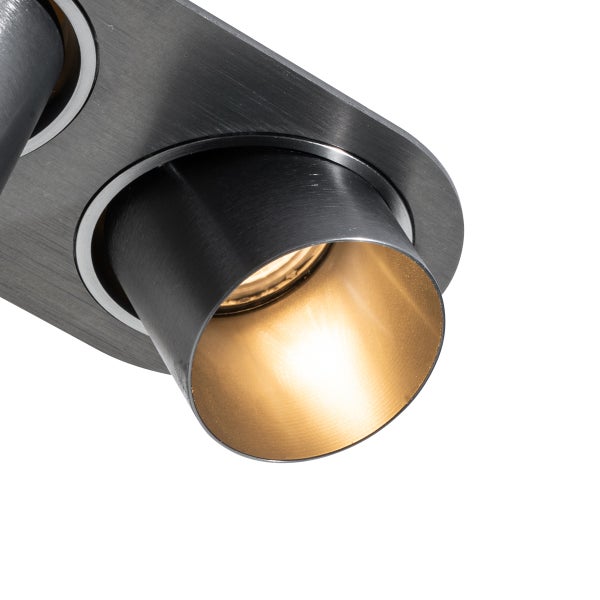 Nahaufnahme eines Deckenstrahlers aus dunkel gebürstetem Metall mit goldener Innenseite und warmem Licht.