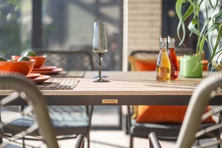 Nahaufnahme eines Gartentischs von Garden Impressions mit Tischplatte in Holzoptik, Geschirr und Stühlen im Außenbereich.