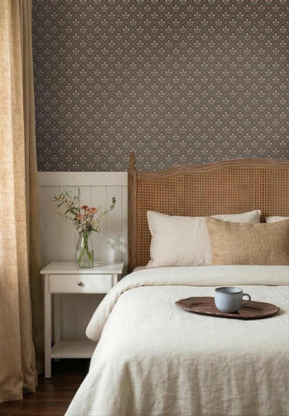 Schlafzimmer mit gemusterter Tapete, weißer Wandvertäfelung, Holzbett mit Wiener Geflecht, weißem Nachttisch und heller Bettwäsche.