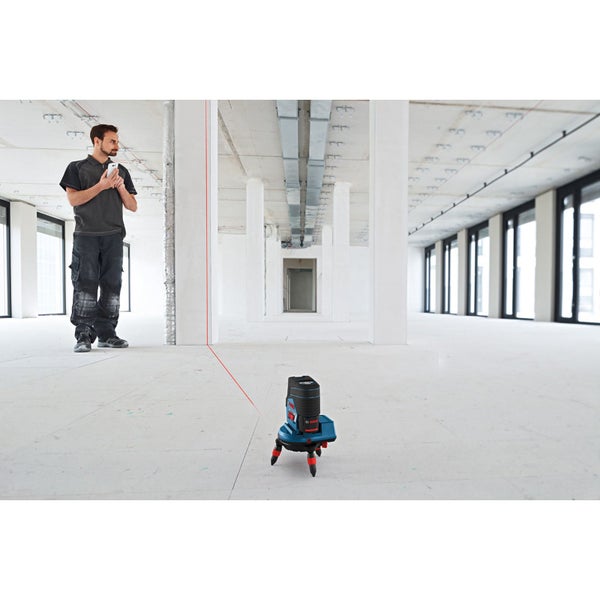 Ein Mann benutzt einen Linienlaser in einem Raum, um eine rote Linie an die Wand zu projizieren. Das Gerät steht auf dem Boden.