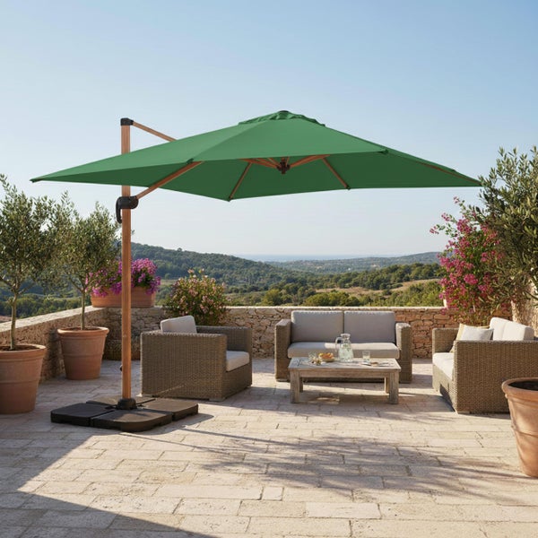 Grüner Ampelschirm auf einer hellen Steinterrasse mit Rattan-Gartenmöbeln und Blick in die Natur.
