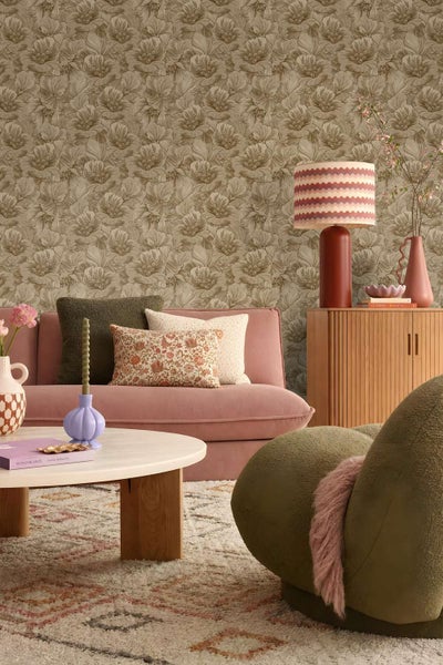 Ein Wohnzimmer mit einer florale Vliestapete, einem rosafarbenen Sofa, einem Couchtisch, einer Kommode und dekorativen Wohnaccessoires.