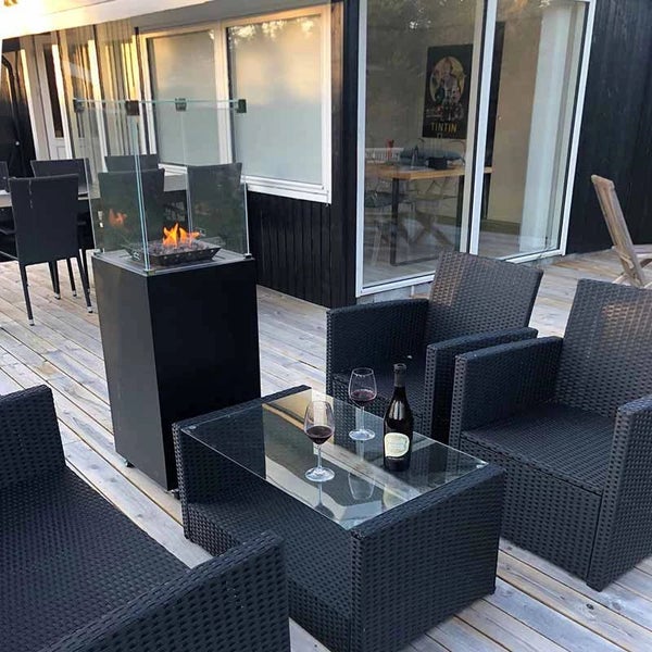 Außenbereich auf einer Holzterrasse mit einer Gas-Feuerstelle, Rattan-Sesseln und einem Couchtisch mit Glasplatte.