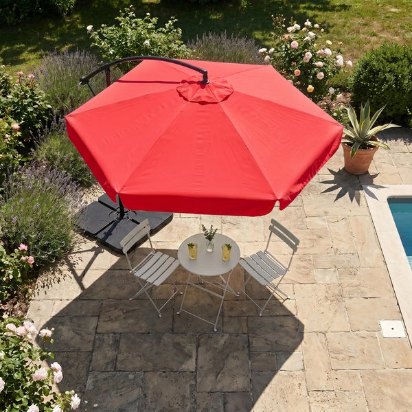 Ein großer roter Ampelschirm über einem weißen Bistro-Set mit zwei Stühlen und einem runden Tisch auf einer Steinterrasse am Pool.