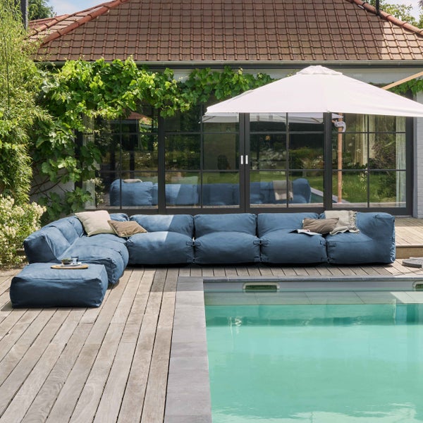 Modernes blaues modulares Outdoor-Lounge-Sofa auf einer Holzterrasse neben einem Pool mit weißem Sonnenschirm und Pflanzen.