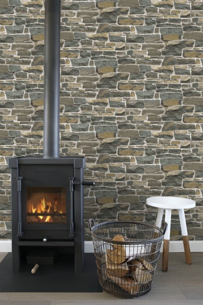 Kaminofen mit Kaminrohr, Holzkorb und Hocker vor Steinwand