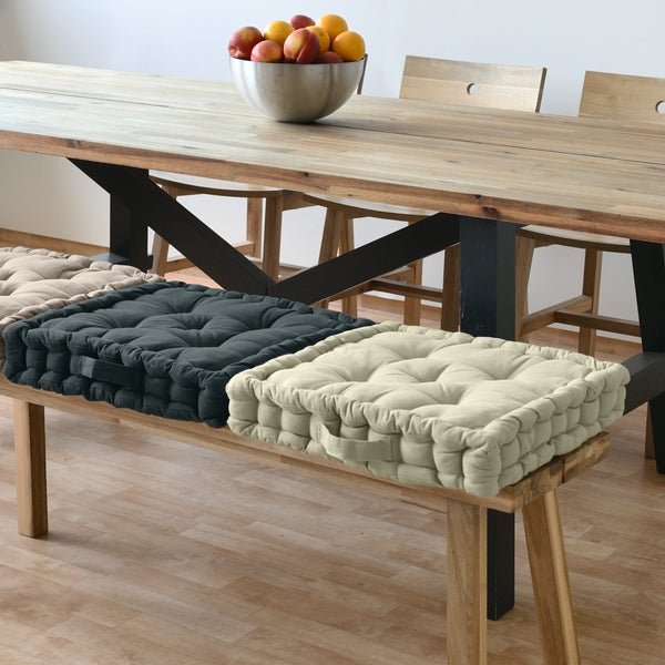 Quadratische Sitzkissen auf einer Holzbank unter einem Esstisch mit Obstschale.