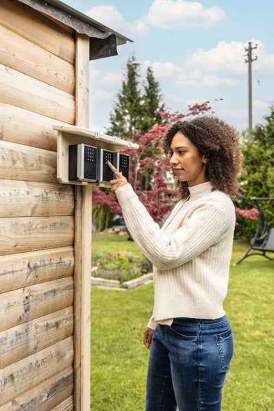 Frau bedient elektronischen ABUS Schlüsseltresor an einer Gartenhütte aus Holz.