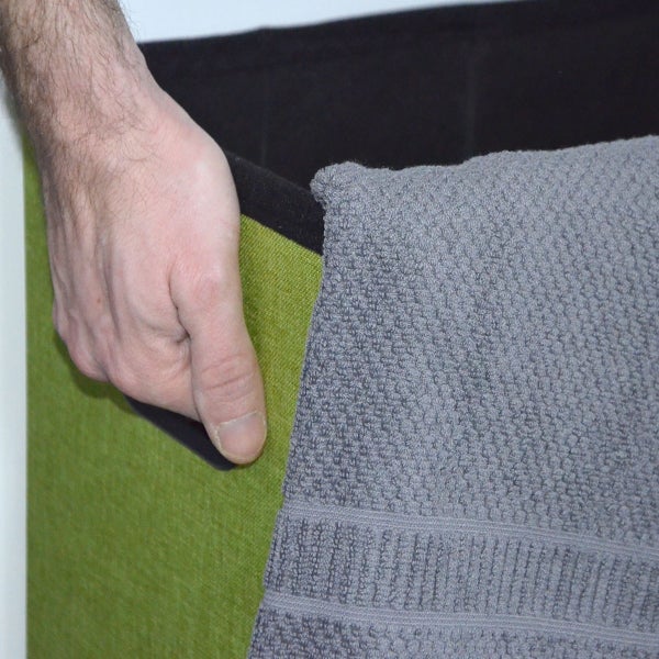 Hand hält den Griff einer grünen Stoff Aufbewahrungsbox mit einem grauen Handtuch über dem Rand.