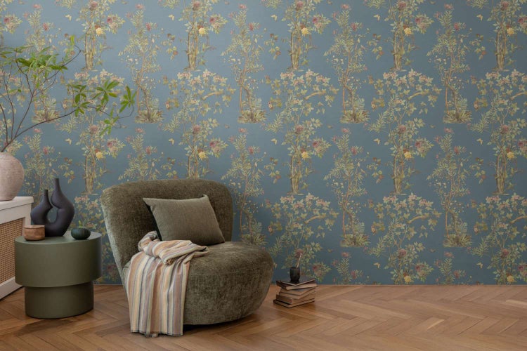 Vliestapete mit floralem Baum- und Blumenmuster in einem elegant eingerichteten Wohnzimmer mit gemütlichem Sessel auf Parkettboden.