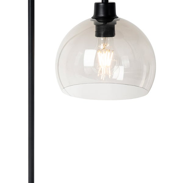 Nahaufnahme einer Lampe mit kuppelförmigem Schirm aus Rauchglas, sichtbarem Leuchtmittel und schwarzem Metallgestell.