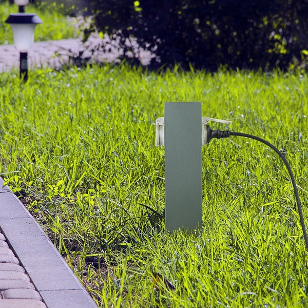 Eckige Energiestation für den Garten auf einem Rasen neben einem Weg, zwei Steckdosen mit Klappdeckeln, eine davon mit eingestecktem Kabel.