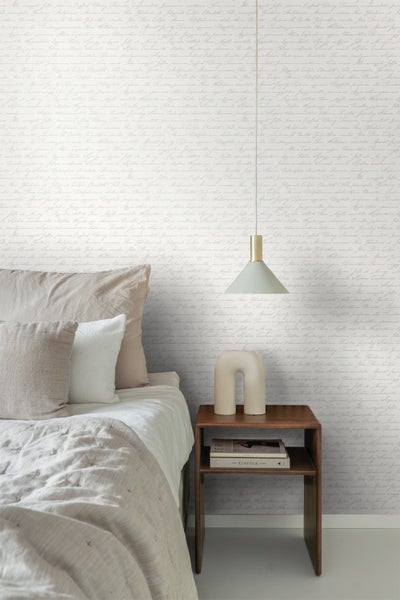 Schlafzimmer mit Bett, Nachttisch, Lampe und Tapete mit Schriftzug