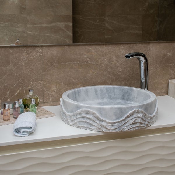 Rundes Aufsatzwaschbecken aus Marmor mit Wellenstruktur, verchromte Armatur und weißer Unterschrank in einem modernen Badezimmer.